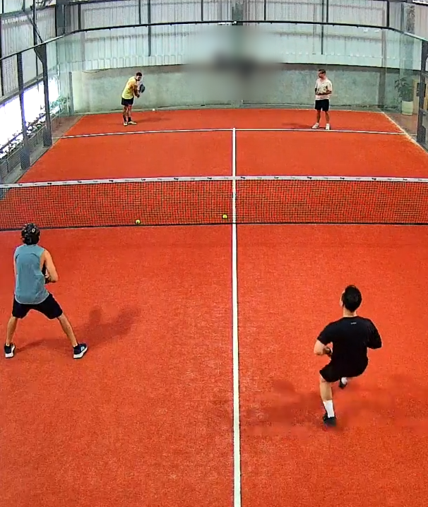 Wide-angle camera view of a padel court with all four players in frame
